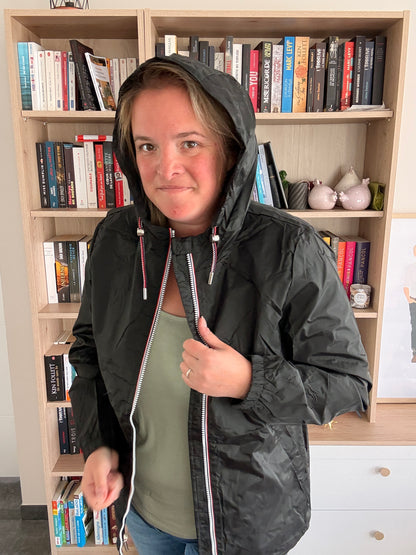 Femme portant l'imperméable court noir Laura Jo avec capuche relevée, cordons tricolores ajustables visibles, veste ouverte