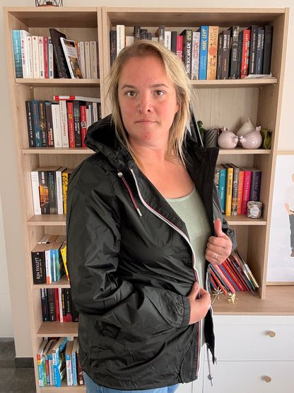 Femme tenant le revers gauche de l'imperméable court noir Laura Jo ouvert, zip tricolore et capuche intégrée visibles