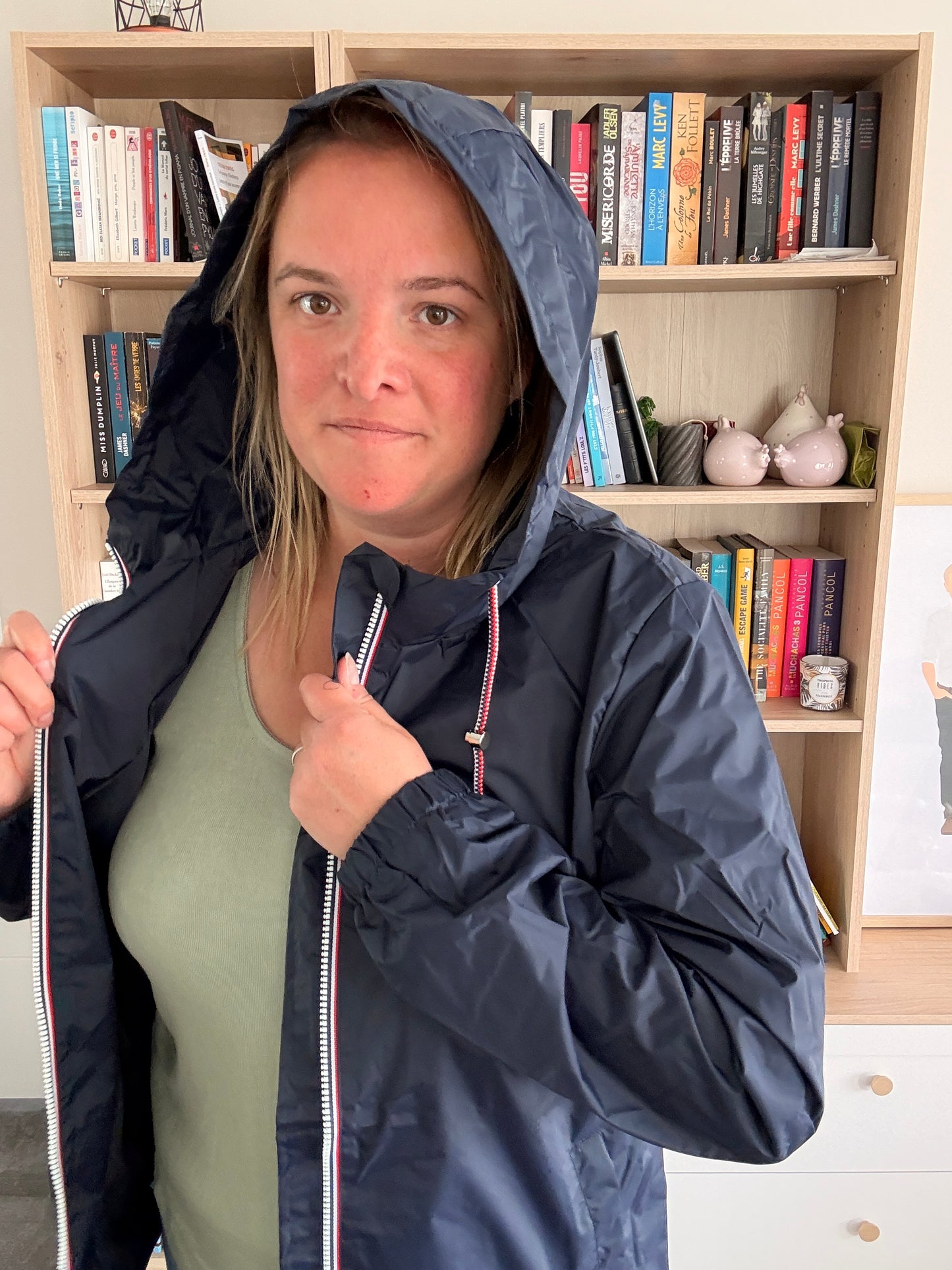 Femme portant l'imperméable mi-long bleu marine Laura Jo avec capuche relevée, veste ouverte tenue à deux mains