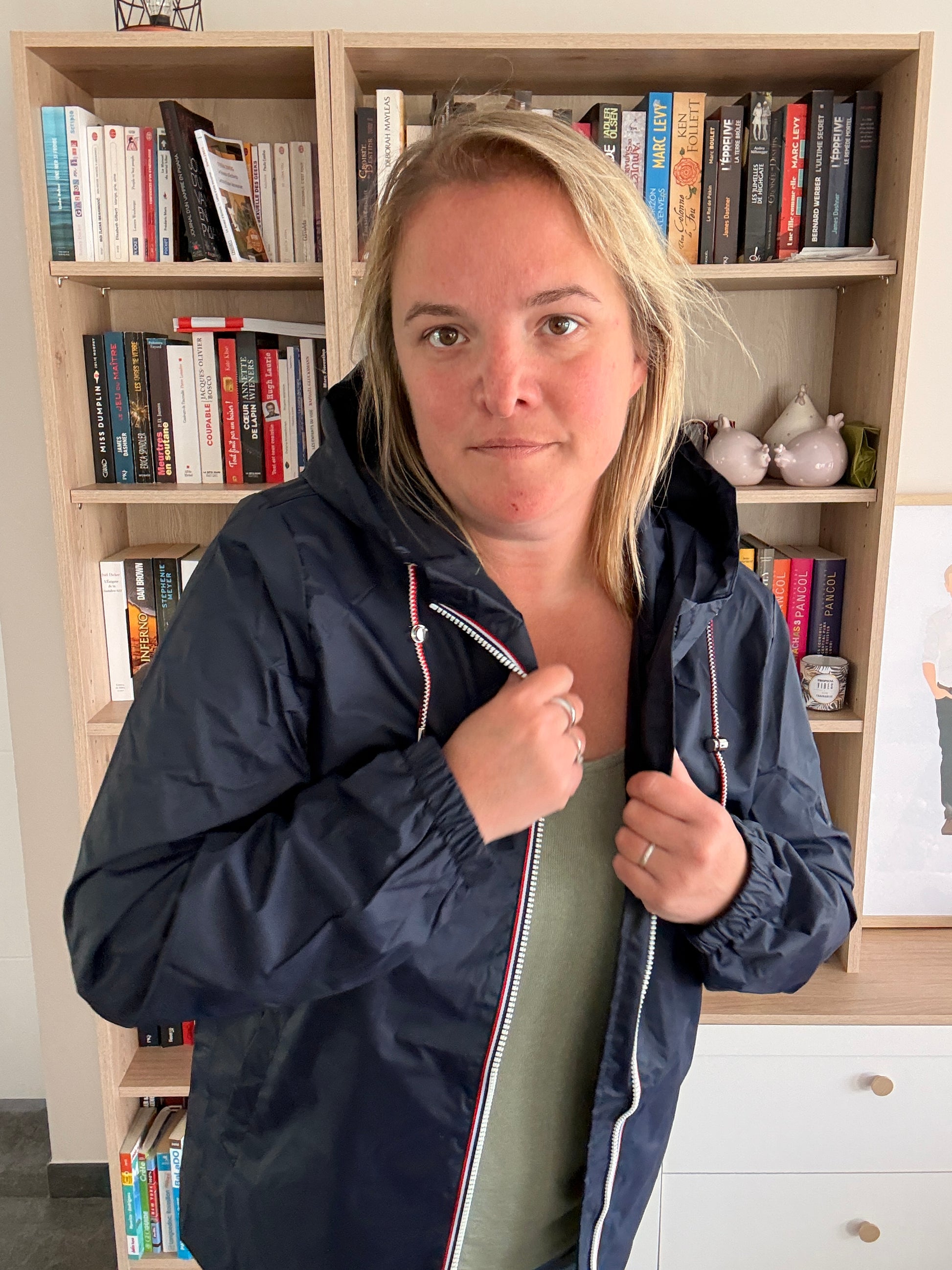 Femme de face portant l'imperméable mi-long bleu marine Laura Jo ouvert, revers tenus à deux mains, zip tricolore visible