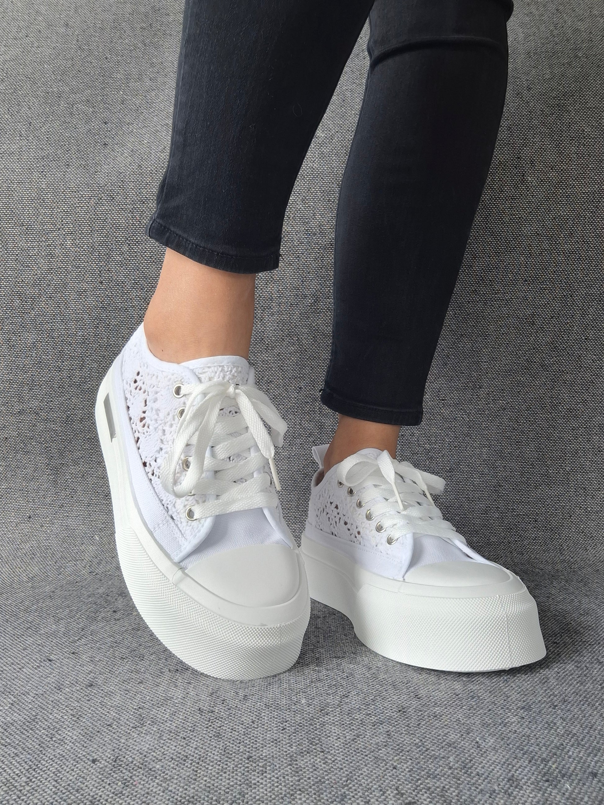 Sneakers blanches à plateforme en dentelle crochetée portées avec un jean noir, semelle épaisse et lacets blancs