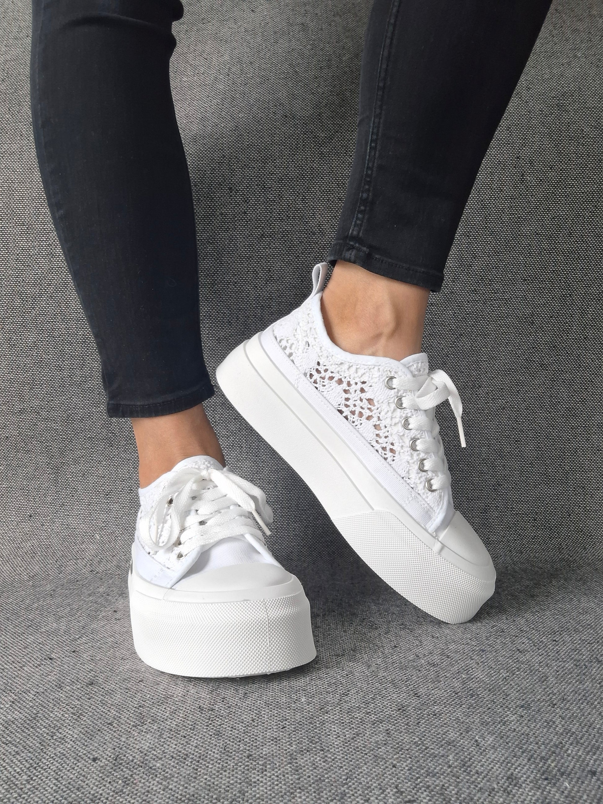Sneakers blanches à plateforme en dentelle crochetée portées avec un jean noir, semelle épaisse et lacets blancs
