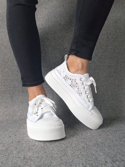 Sneakers blanches à plateforme en dentelle crochetée portées avec un jean noir, semelle épaisse et lacets blancs