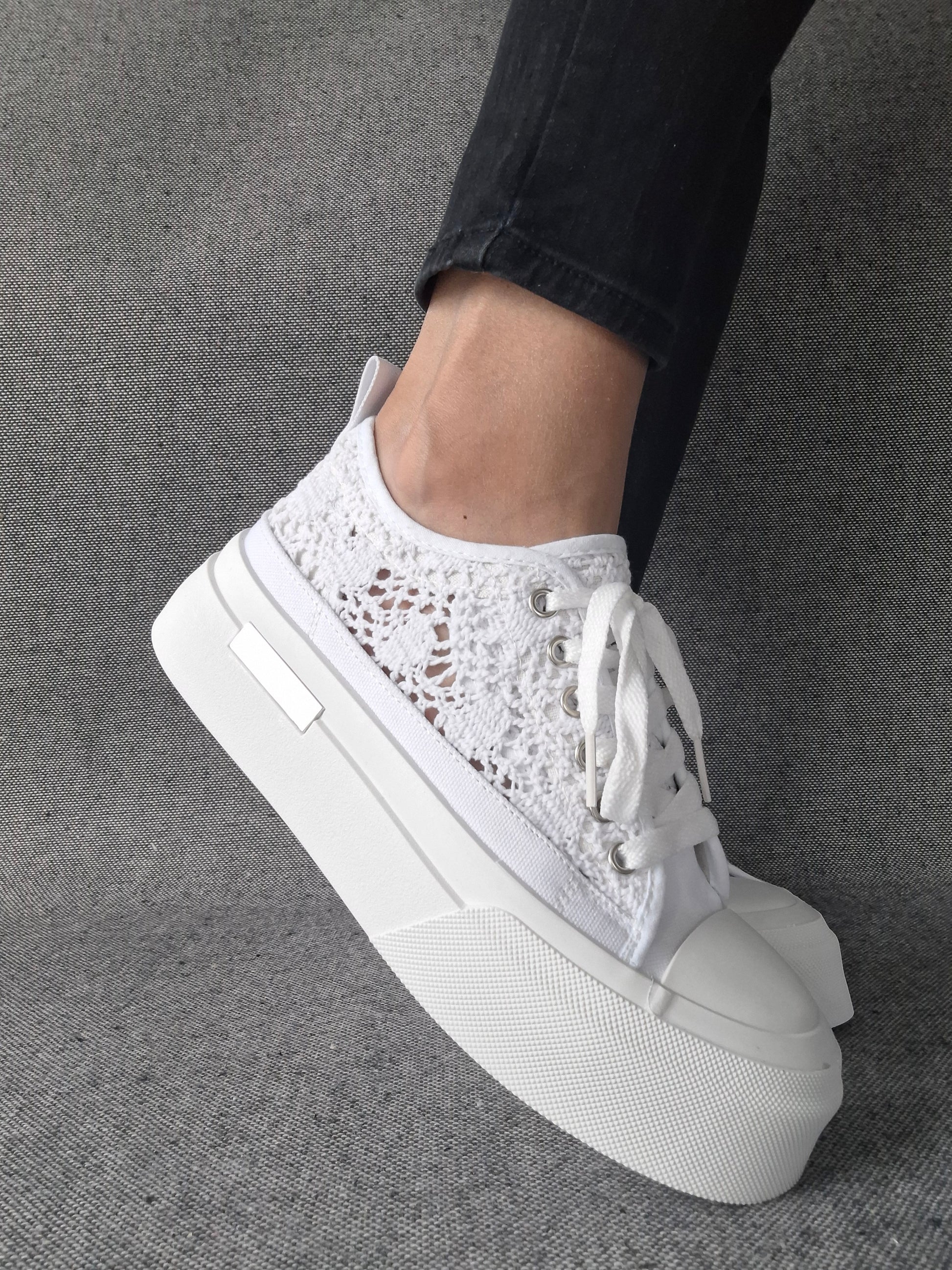 Sneakers blanches à plateforme en dentelle crochetée portées avec un jean noir, semelle épaisse et lacets blancs