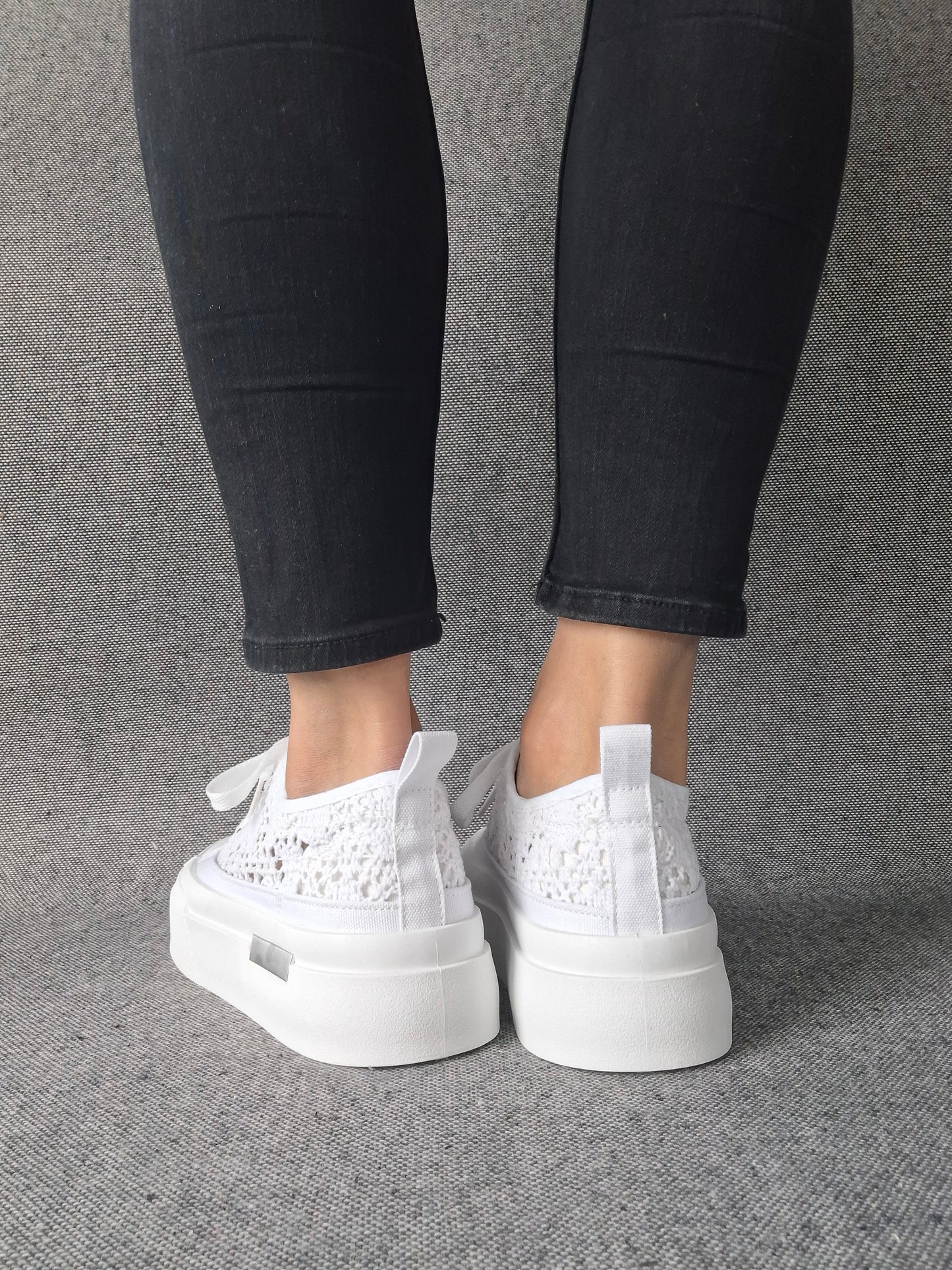 Vue arrière de sneakers blanches à plateforme en dentelle crochetée portées avec un jean noir