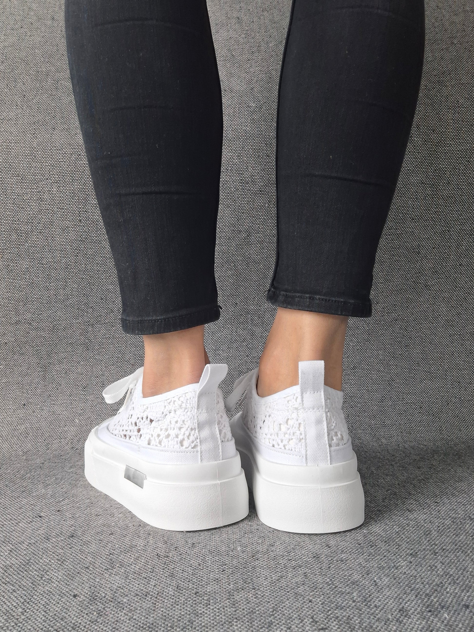 Vue arrière de sneakers blanches à plateforme en dentelle crochetée portées avec un jean noir