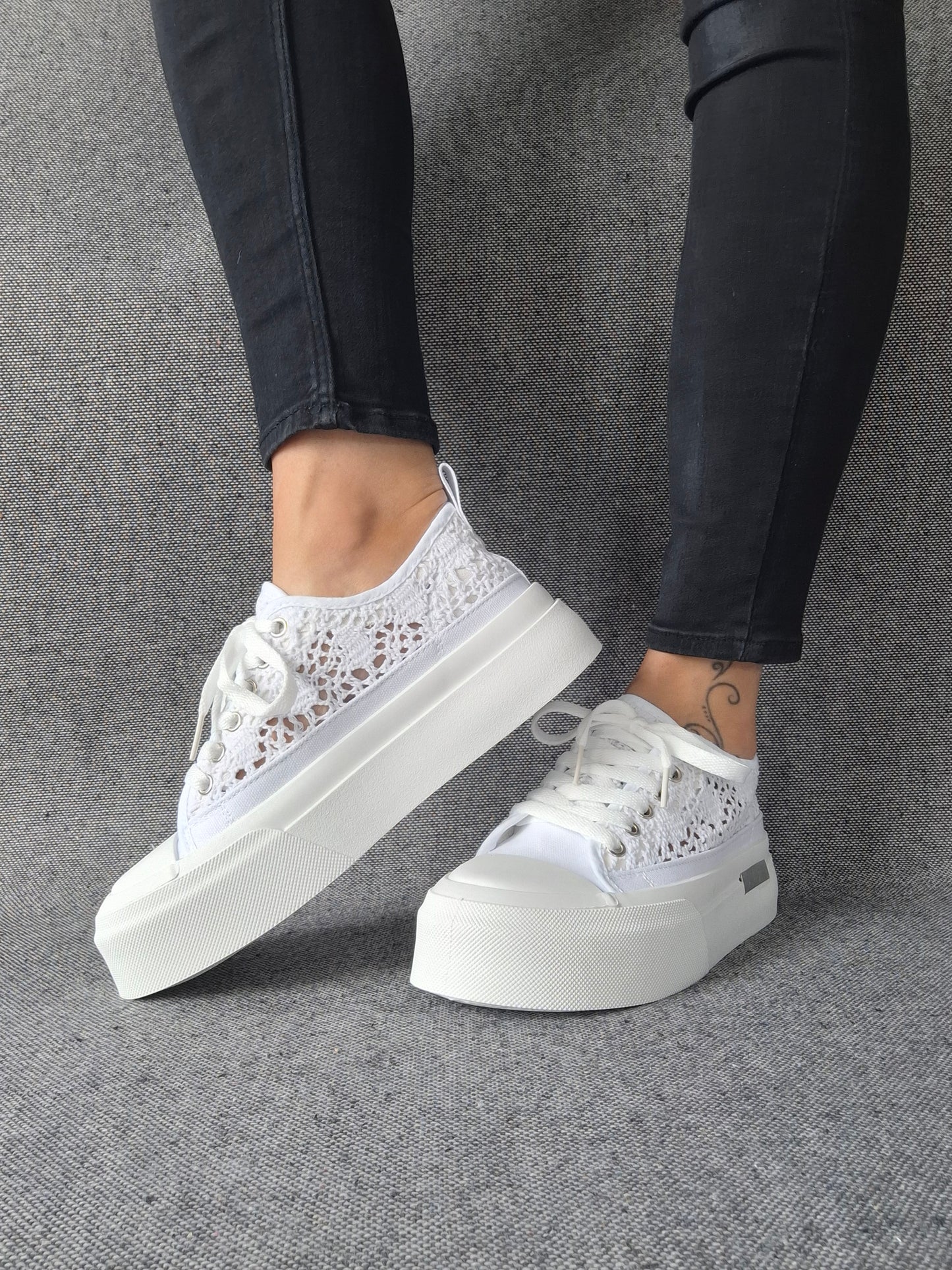 Sneakers blanches à plateforme en dentelle crochetée portées avec un jean noir, semelle épaisse et lacets blancs