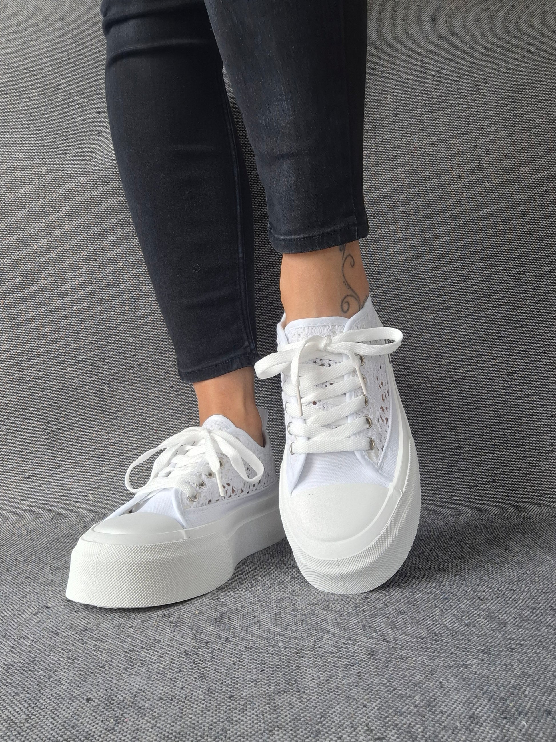Sneakers blanches à plateforme en dentelle crochetée portées avec un jean noir, semelle épaisse et lacets blancs