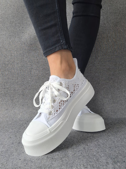 Sneakers blanches à plateforme en dentelle crochetée portées avec un jean noir, semelle épaisse et lacets blancs