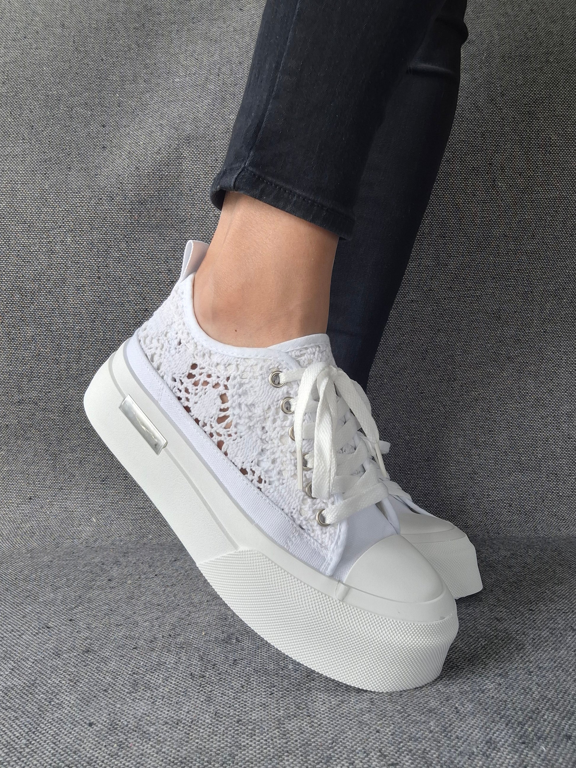 Sneakers blanches à plateforme en dentelle crochetée portées avec un jean noir, semelle épaisse et lacets blancs