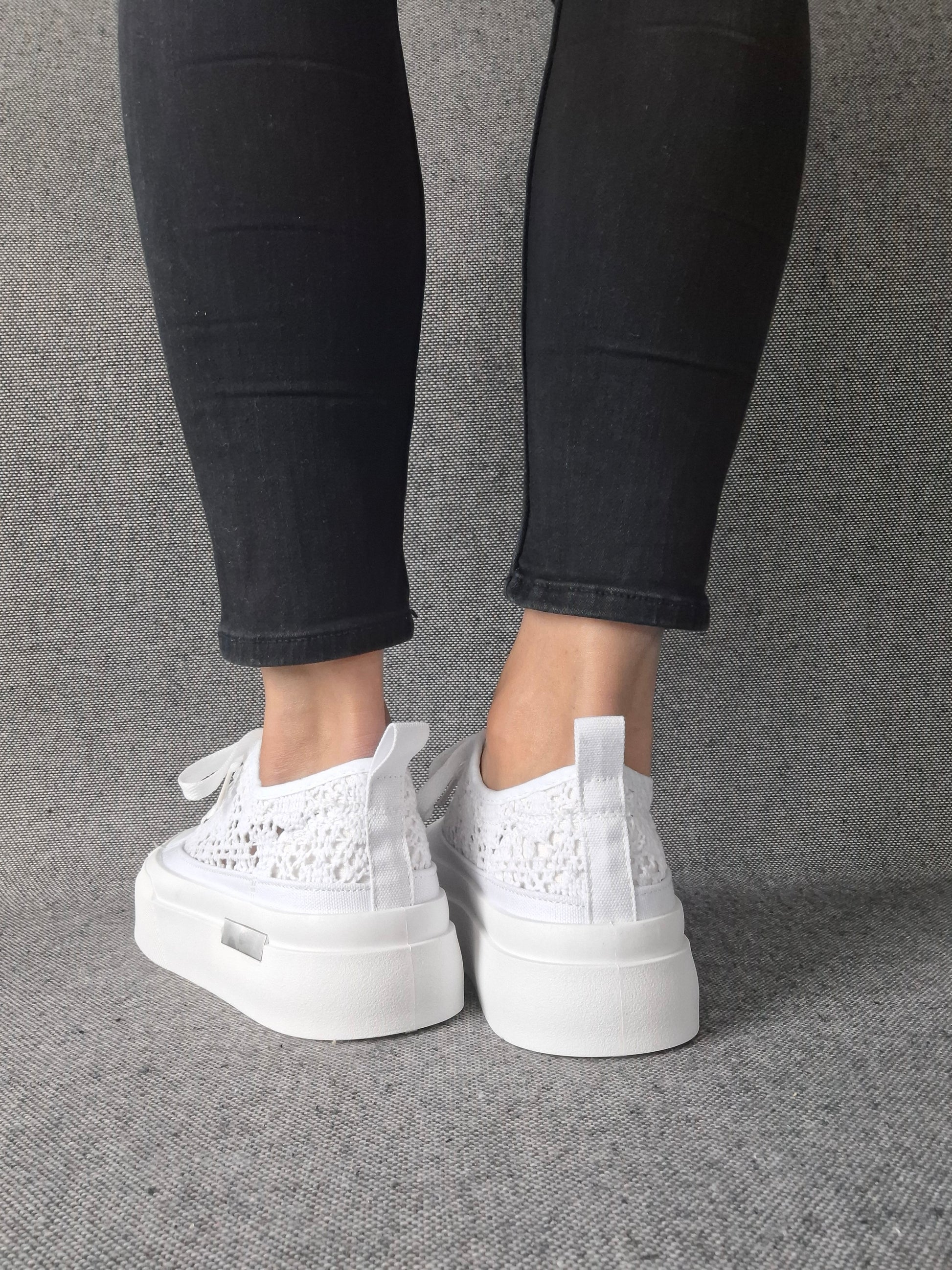 Vue arrière de sneakers blanches à plateforme en dentelle crochetée portées avec un jean noir