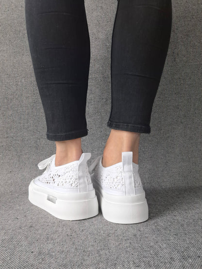 Vue arrière de sneakers blanches à plateforme en dentelle crochetée portées avec un jean noir