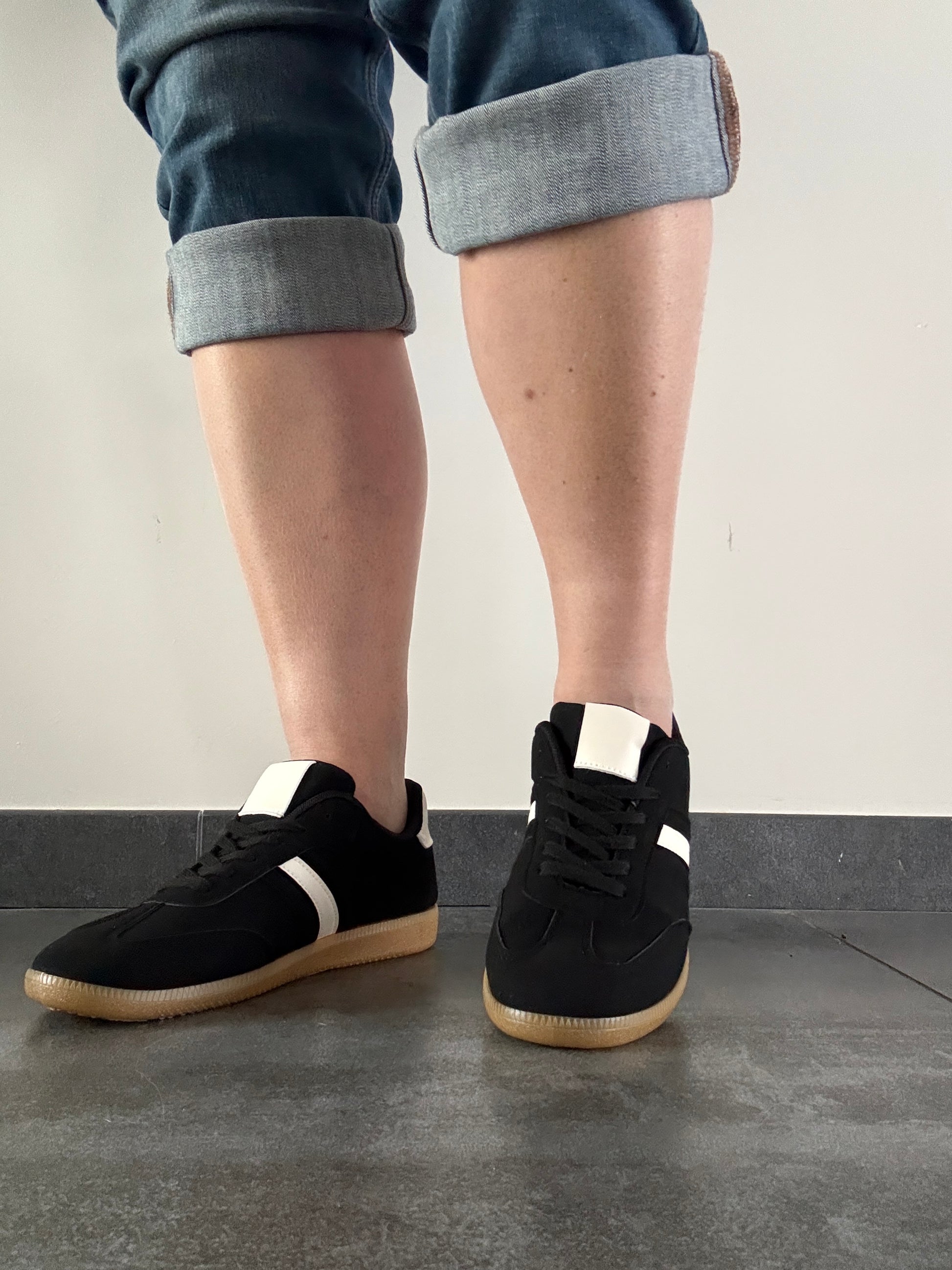 Baskets basses noires bande blanche femme style sneakers campus portées avec un jean retroussé, semelle gomme caramel