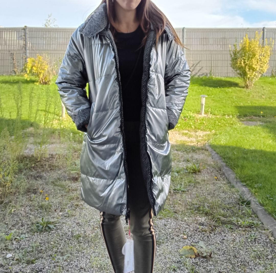 Woman wearing a long reversible silver quilted waterproof coat outdoors from Le Petit Placard.