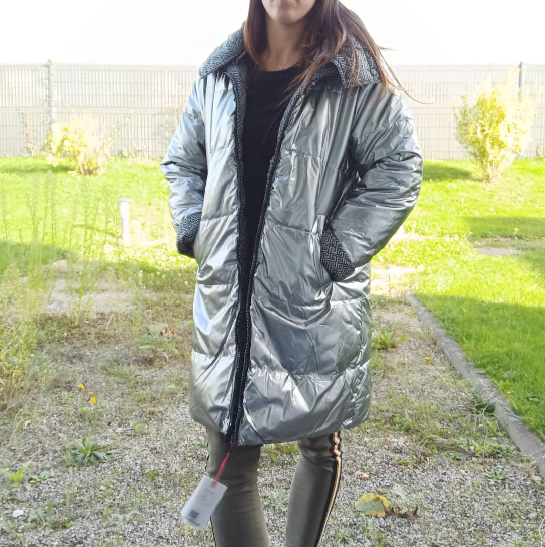 Woman wearing long silver reversible waterproof puffer coat from Le Petit Placard outdoors.