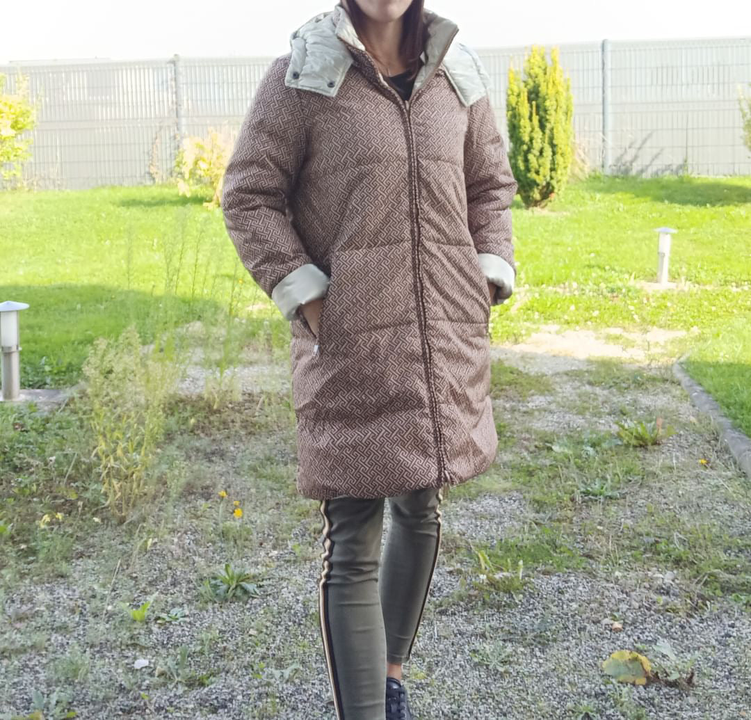Woman wearing Escandelle reversible long waterproof quilted brown coat, outdoor setting