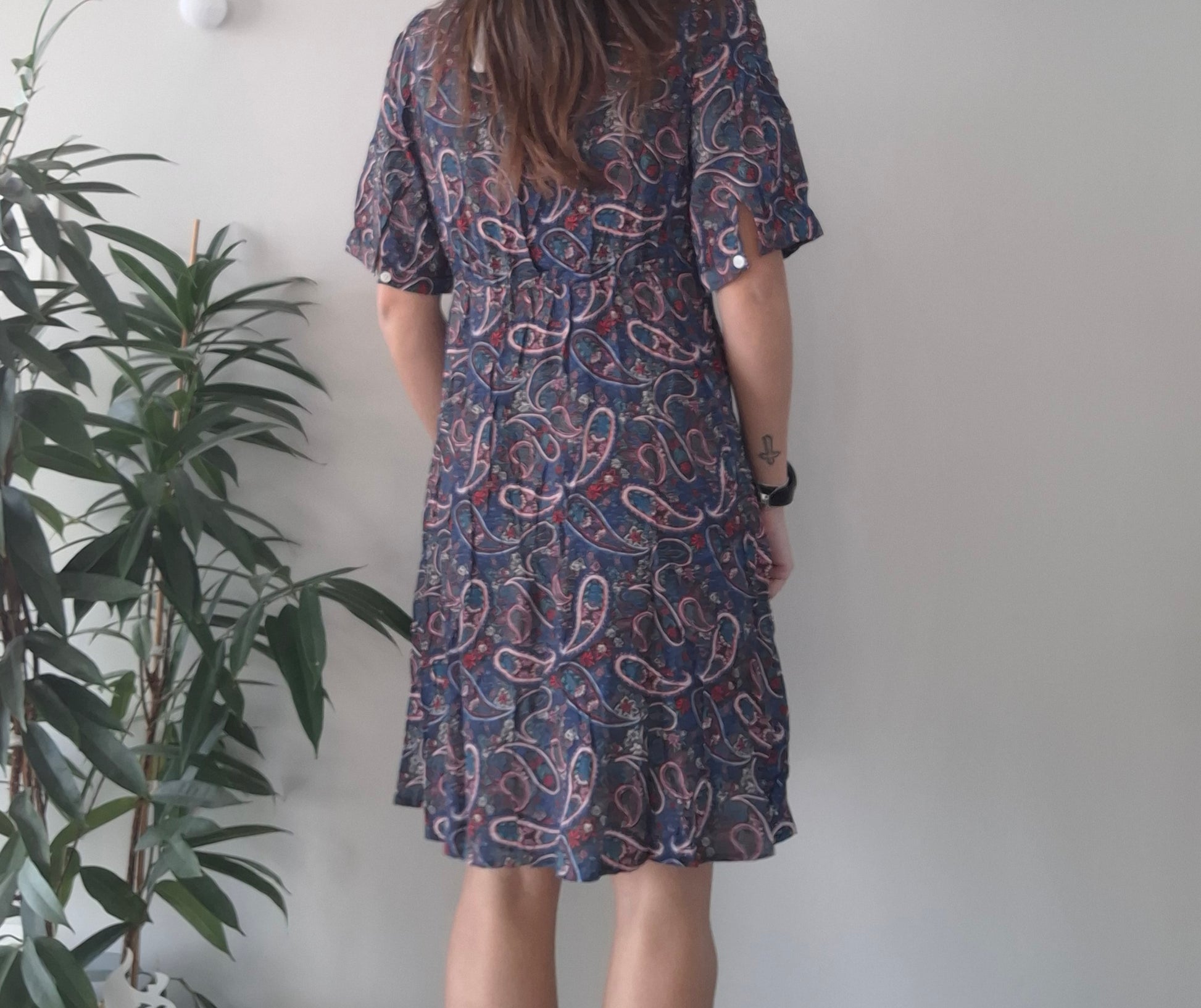 Woman in a paisley print dress standing indoors near a green plant, Le Petit Placard fashion