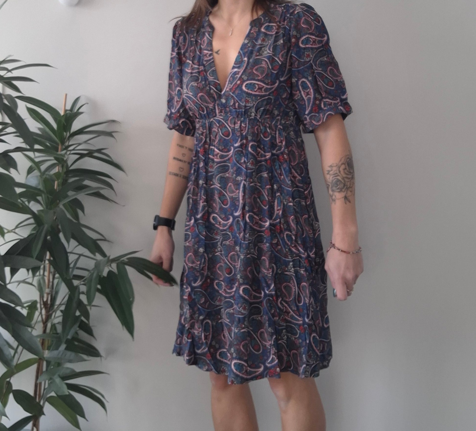 Woman wearing paisley print dress with short sleeves, standing indoors by a plant
