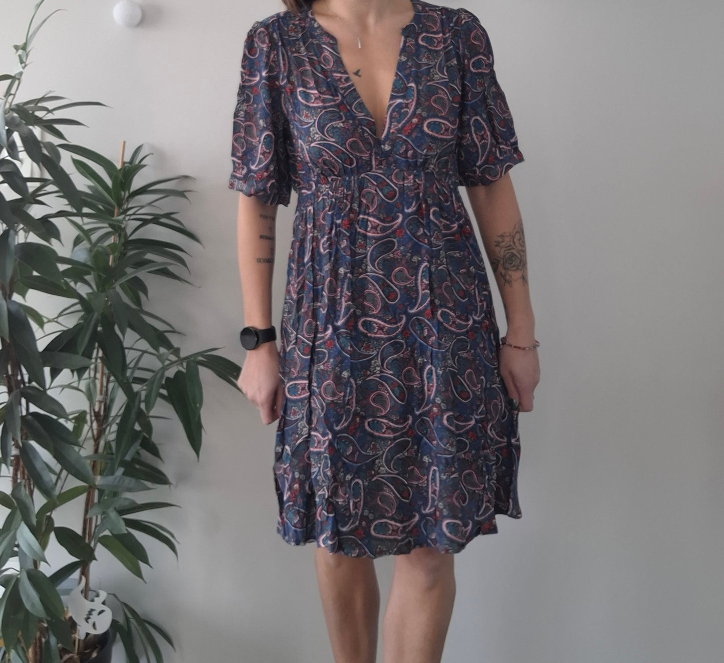 Woman in paisley print dress by Le Petit Placard, standing indoors beside a plant