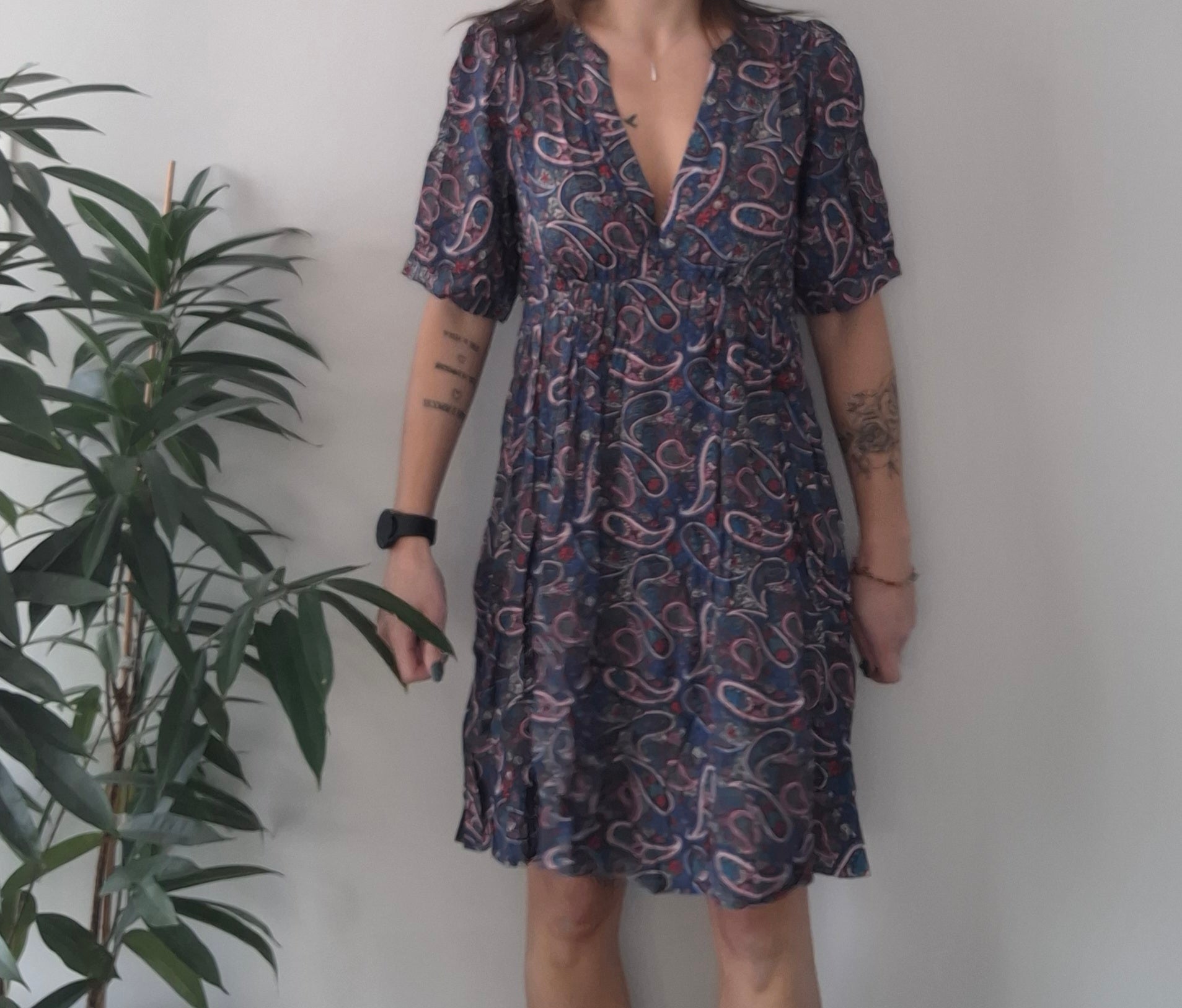 Woman wearing paisley print dress from Le Petit Placard, standing by green plant