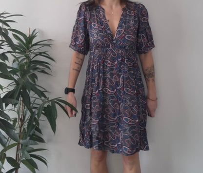 Woman wearing paisley print dress from Le Petit Placard, standing by green plant