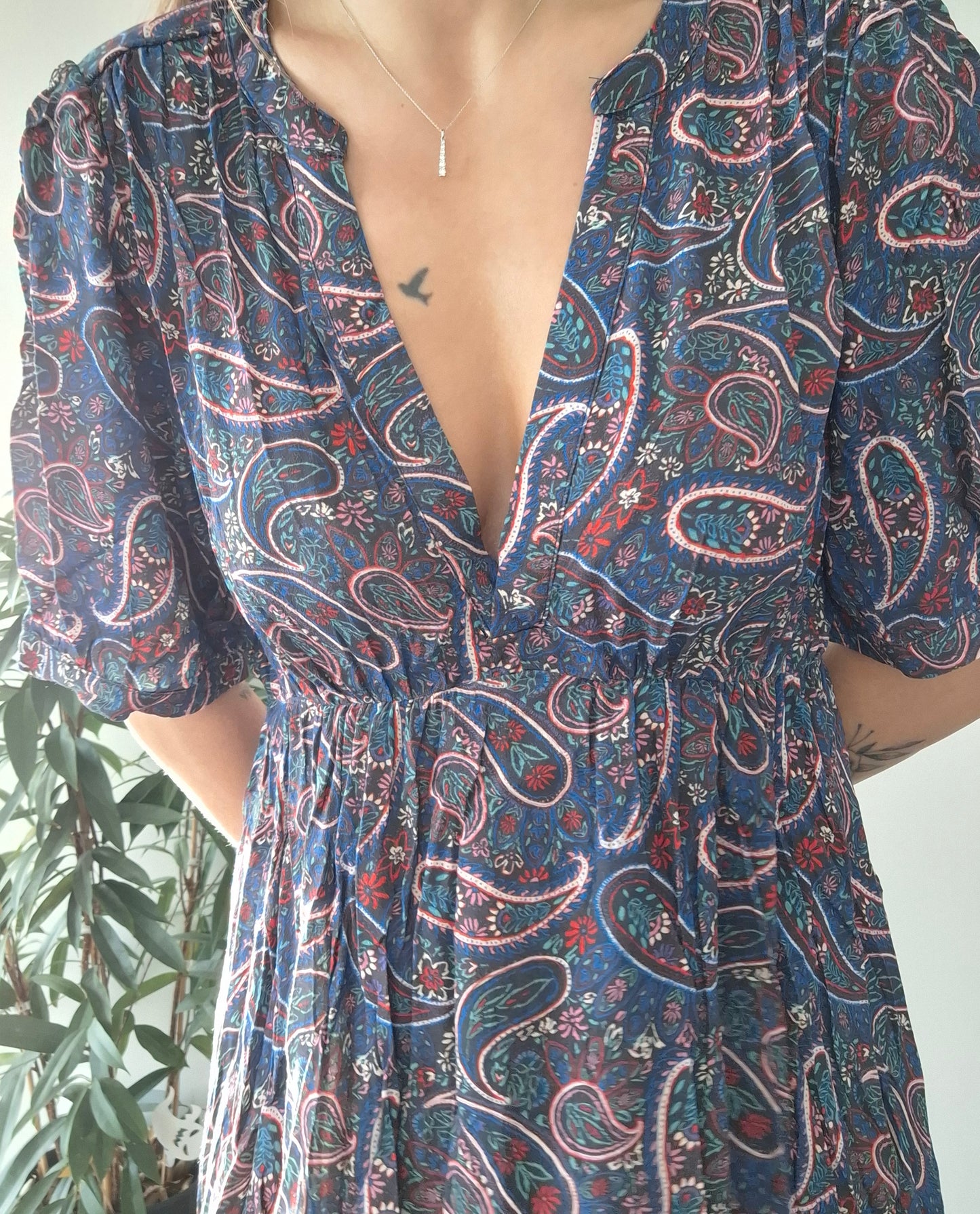 Woman in a paisley print dress with deep neckline, wearing a delicate necklace, Le Petit Placard