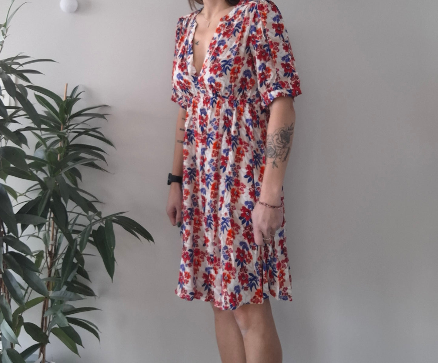 Woman wearing a floral summer dress with red and blue patterns, standing indoors by a plant