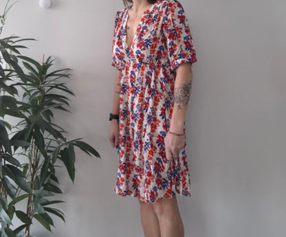 Woman wearing a floral summer dress with red and blue patterns, standing indoors by a plant