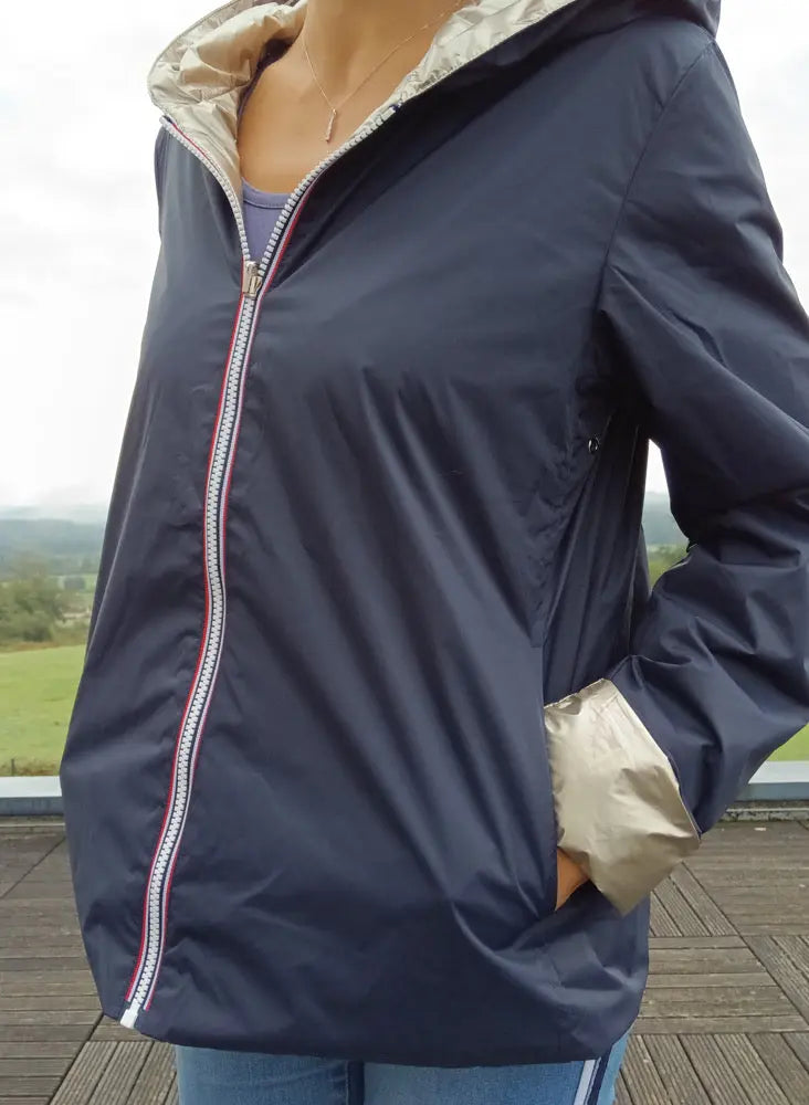 Imperméable réversible court bleu marine avec doublure et capuche beiges, fermeture zippée contrastée; femme en extérieur.
