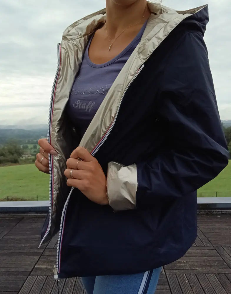 Imperméable réversible court bleu marine doré femme porté en plein air, avec capuche, zips visibles et manches contrastées dorées.