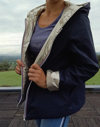 Imperméable réversible court bleu marine doré femme porté en plein air, avec capuche, zips visibles et manches contrastées dorées.