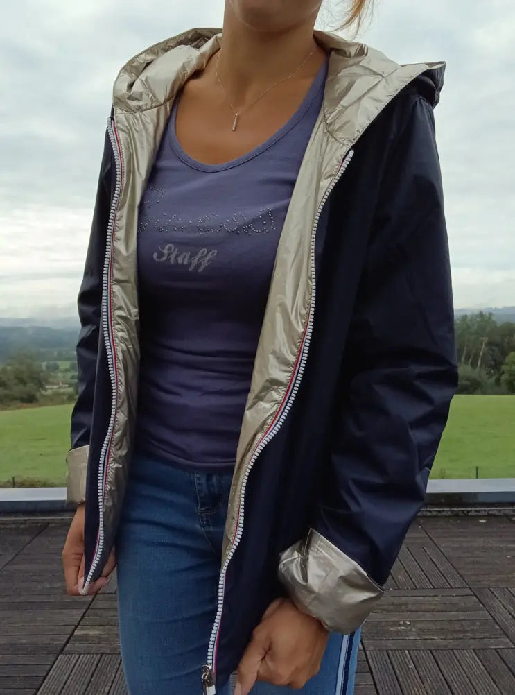 Imperméable réversible court bleu marine doré pour femme, portée ouverte sur une chemise bleue et jean, avec capuche.