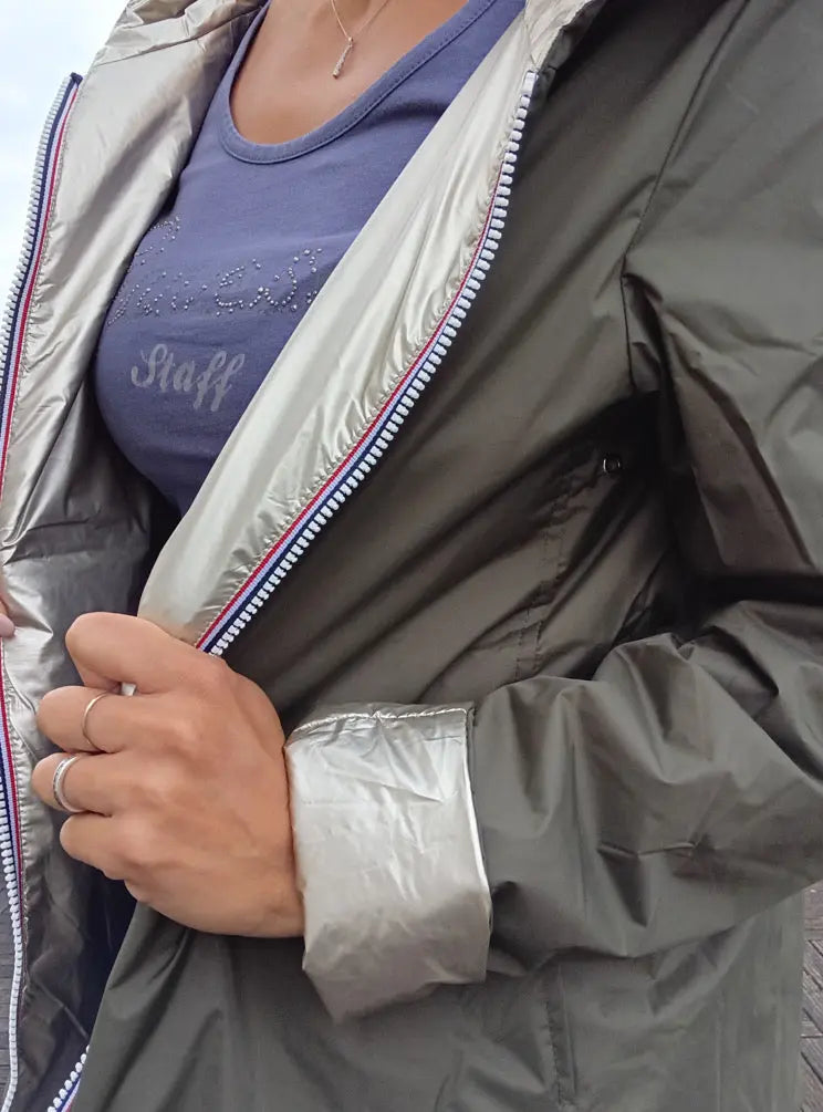 Imperméable réversible court kaki doré pour femme, fermeture éclair bleue, mannequin montrant l’intérieur argenté et le revers kaki.
