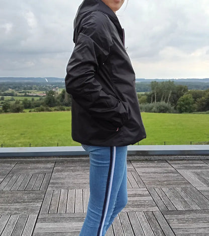 Imperméable réversible court noir doré femme Laura Jo Mi-Saison portée en extérieur avec jeans à rayure, paysage verdoyant en arrière-plan.