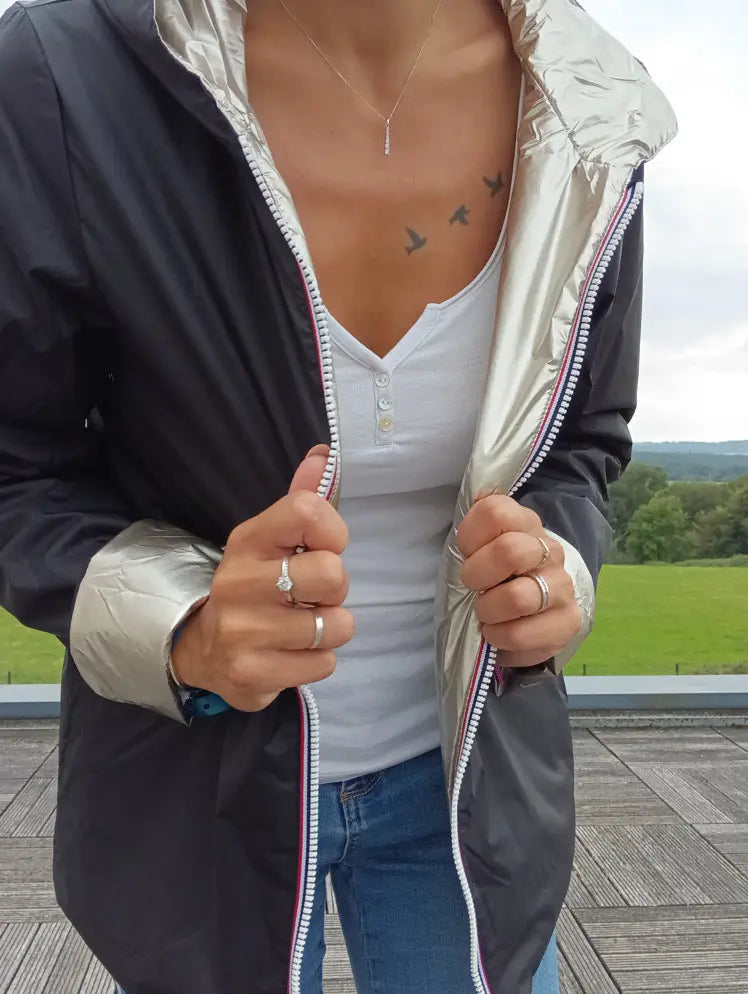 Imperméable réversible court noir doré femme, fermeture éclair visible, white top et tatouage oiseaux sur le décolleté, manches à doublure dorée, portant bagues et collier.