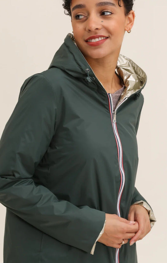 Laura Jo - Veste imperméable réversible vert forêt / doré, coupe courte avec capuche, fermeture éclair centrale à rubans tricolores, doublure sombre, manches pliées, portée en plein air. 