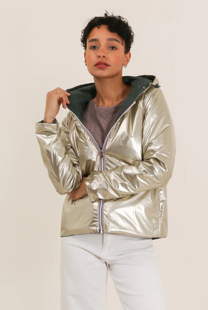 Veste imperméable réversible vert forêt / doré, coupe courte avec capuche, fermeture éclair, doublure sombre, manches pliées, portée en plein air. Laura Jo