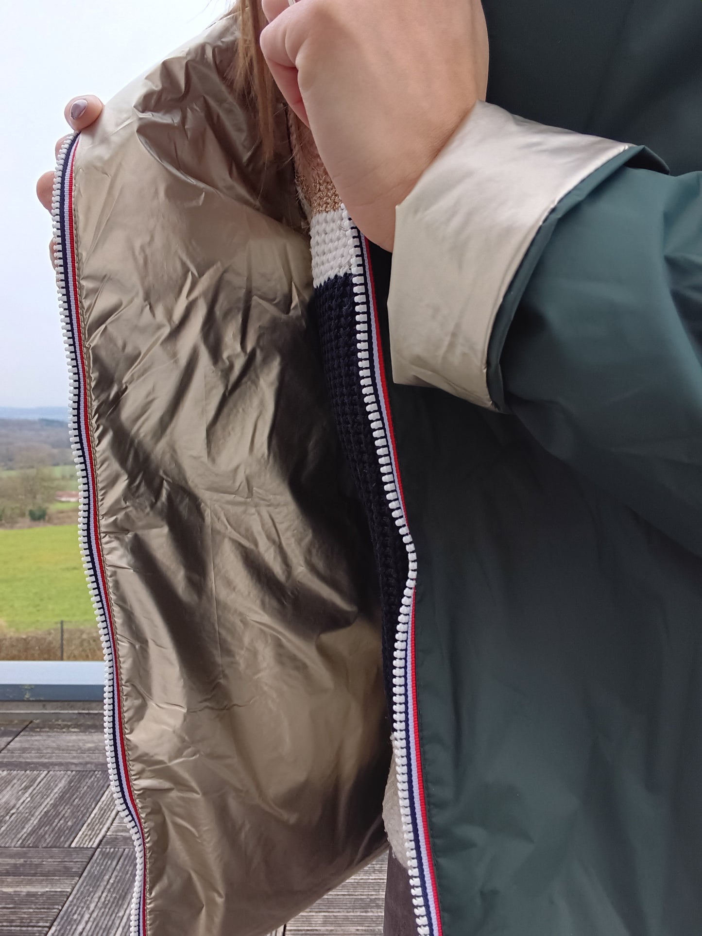 Veste imperméable réversible vert forêt / doré, coupe courte avec capuche, fermeture éclair centrale à rubans tricolores, doublure sombre, manches pliées Laura Jo