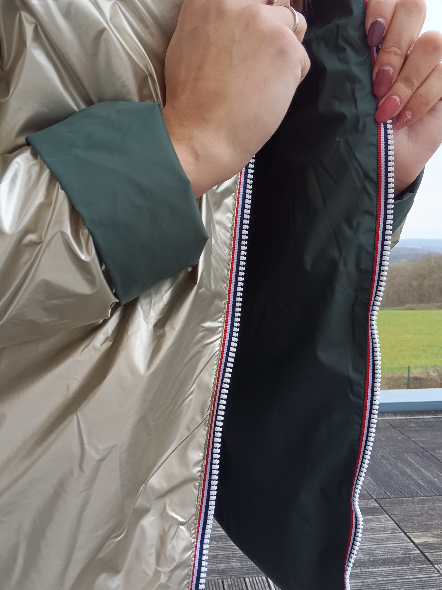 Veste imperméable réversible doré / vert forêt, coupe courte avec capuche, fermeture éclair centrale à rubans tricolores, doublure sombre, manches pliées. Laura Jo