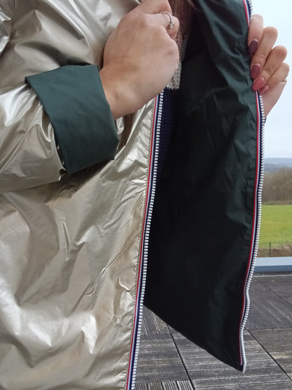 Veste imperméable réversible doré / vert forêt, coupe courte avec capuche, fermeture éclair centrale à rubans tricolores, doublure sombre, manches pliées, portée en plein air. Laura Jo