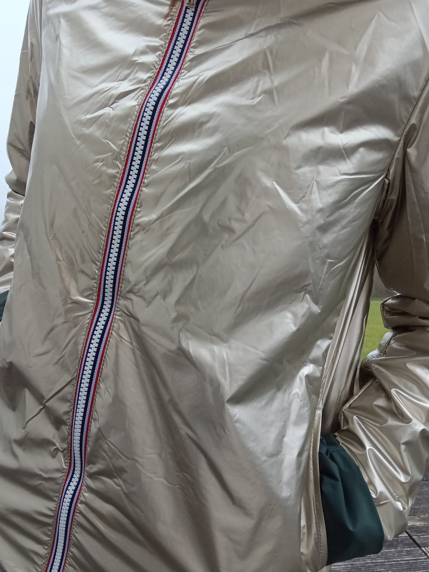 Veste imperméable réversible doré, coupe courte avec capuche, fermeture éclair centrale, doublure sombre, manches pliées, portée en plein air. Laura Jo