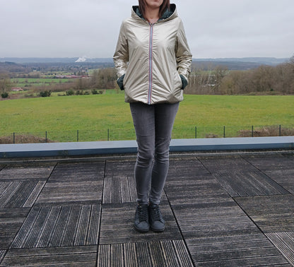 Imperméable réversible court couleur beige doré avec capuche, garnissage ouate, porté par une personne debout sur une terrasse, paysage rural en arrière-plan.