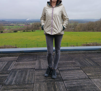 Veste imperméable réversible beige clair, coupe courte avec capuche, fermeture éclair centrale à rubans tricolores, doublure sombre, manches pliées, portée en plein air. Laura Jo 