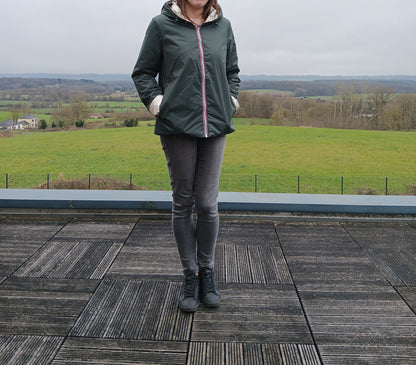 Laura Jo – imperméable réversible court vert forêt avec intérieur doré et garnissage en ouate, vue de femme debout sur terrasse ouverte au paysage rural.