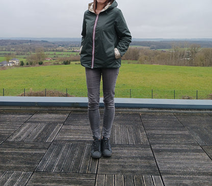Imperméable réversible vert forêt avec garniture en ouate, person standing outdoors sur terrasse, avec paysage rural en arrière-plan.