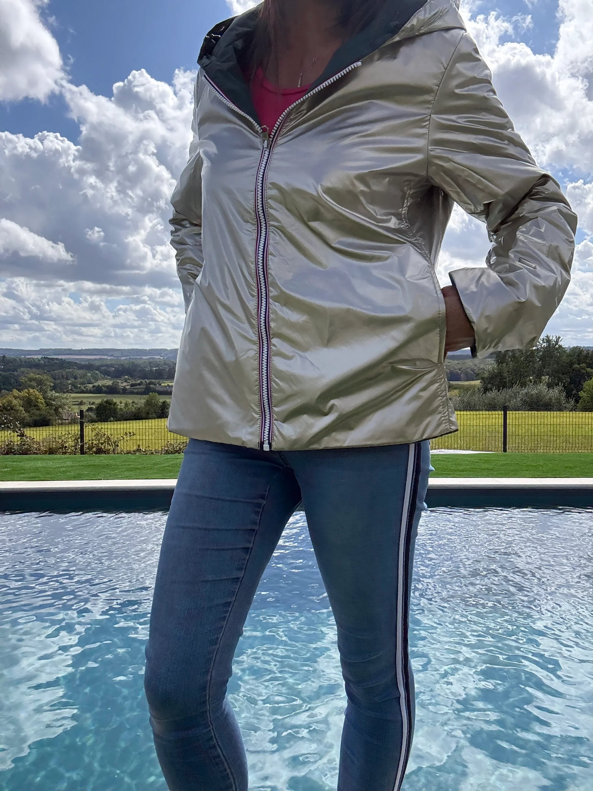 Laura Jo imperméable réversible court en garnissage ouate, couleur vert forêt et doré, veste légère portée près d’une piscine en extérieur.