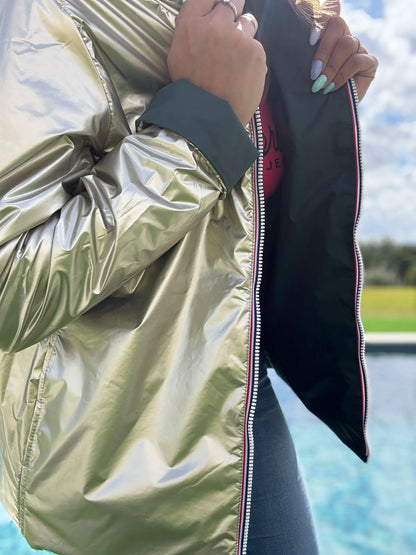 Demme vestière réversible: manteau court argenté brillant avec doublure noire, fermeture éclair argentée, manche et poignet vert foncé, personne ajustant le col près d’un lac.