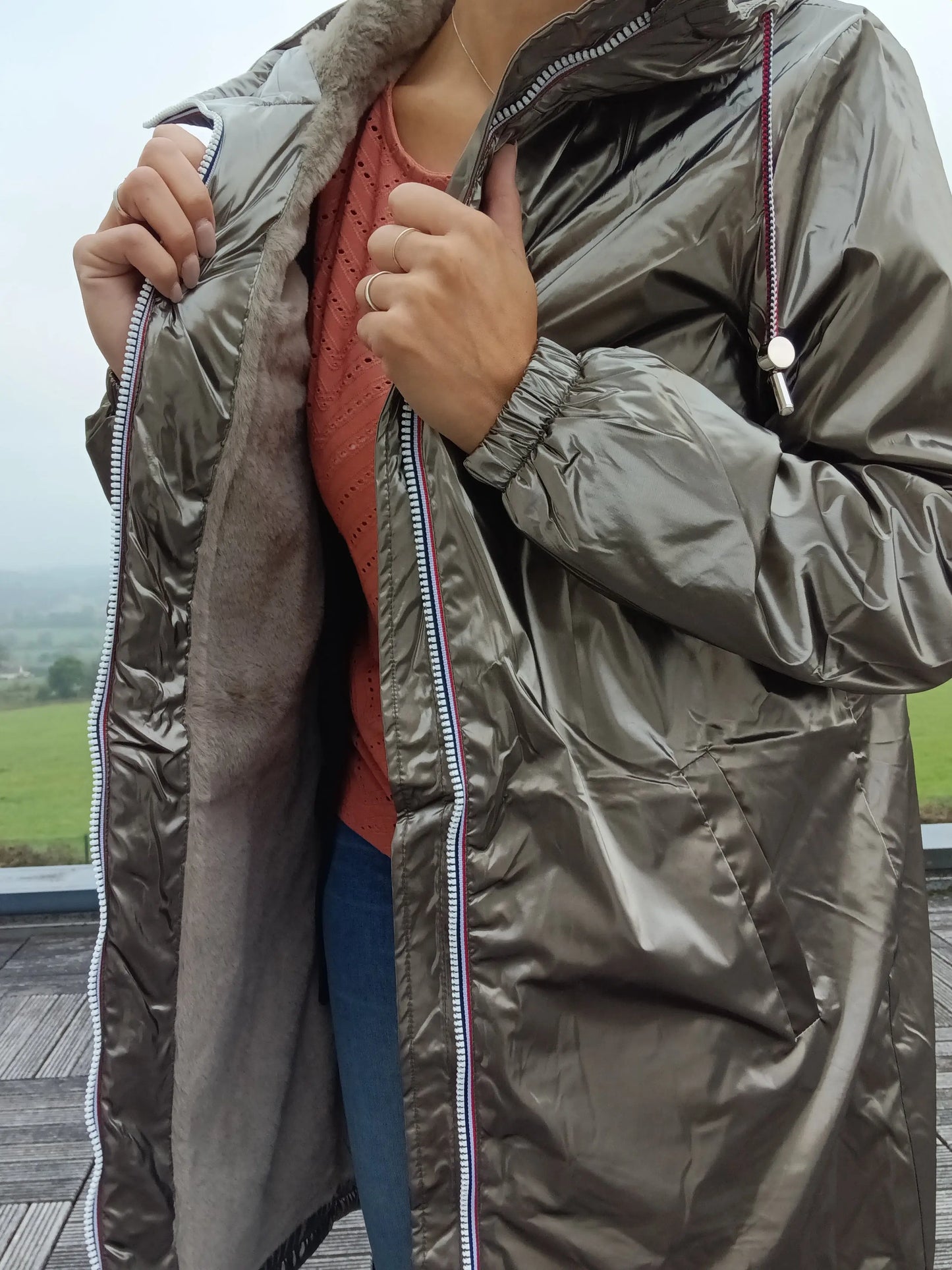 Woman wearing shiny bronze Laura Jo raincoat with faux fur lining, outdoor terrace setting