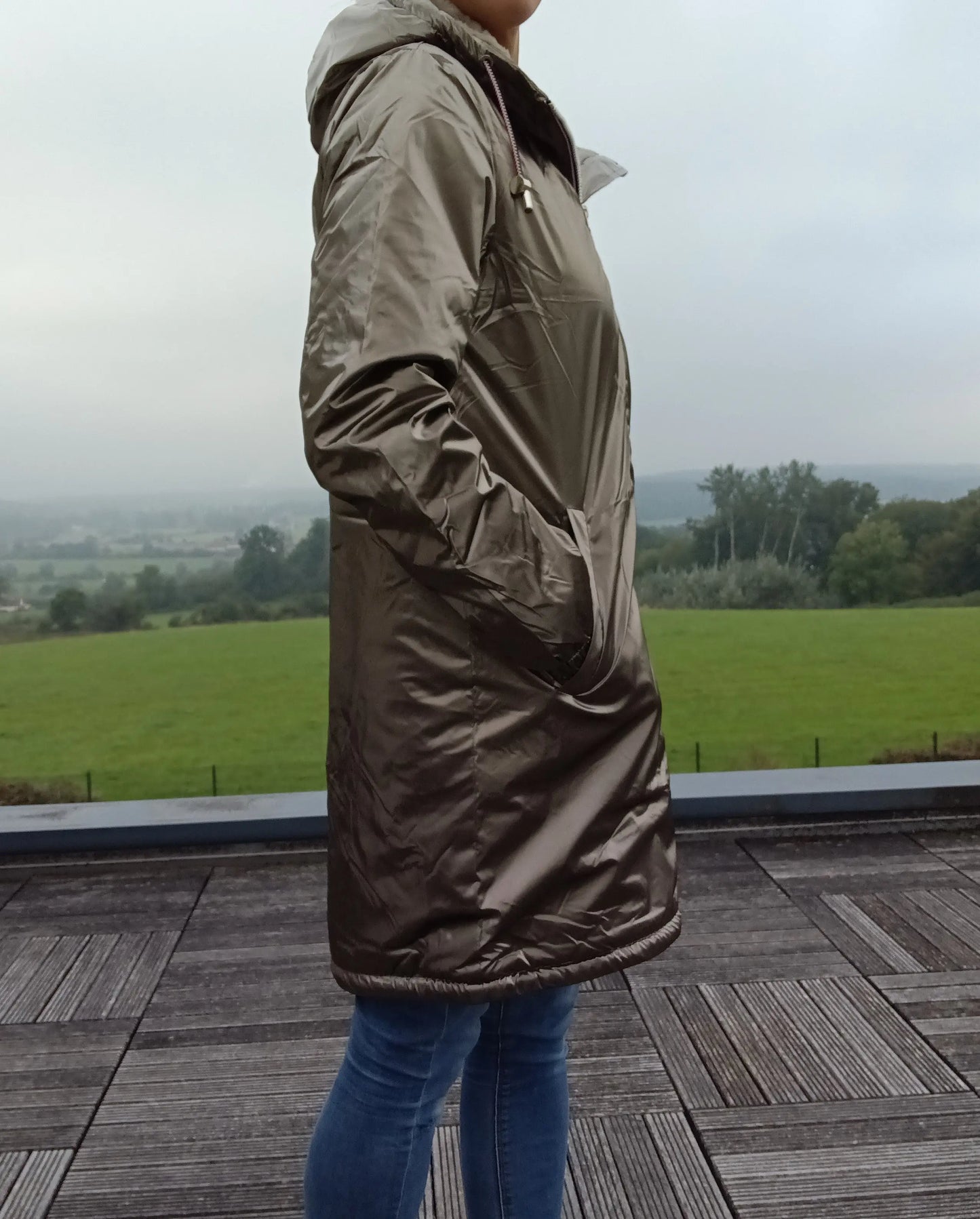 Woman wearing bronze Laura Jo raincoat from Le Petit Placard on terrace with countryside view