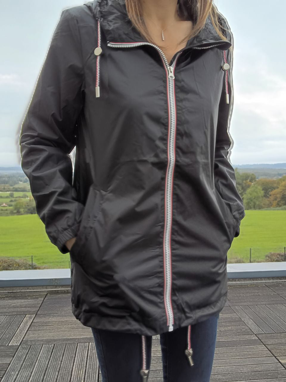 Woman wearing Laura Jo black raincoat with striped zipper, outdoor terrace, Le Petit Placard